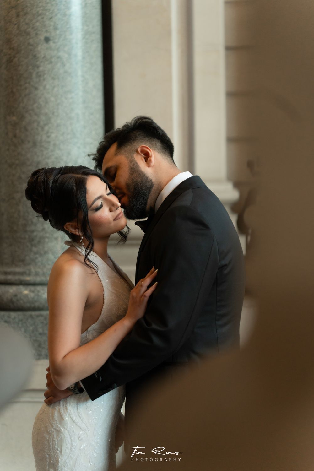 Romantic wedding portrait showing intimate moment between couple in elegant attire against classical column backdrop.