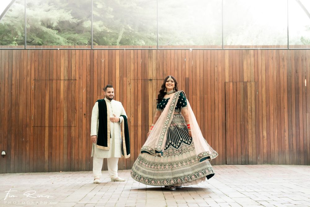 A couple in traditional Indian wedding attire poses in front of a wooden wall during their outdoors photo session.