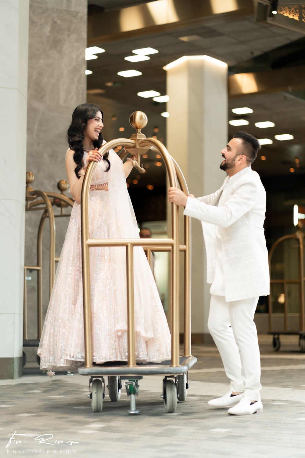 A playful moment captured with a luggage cart in a grand hotel lobby with marble columns and decorative lighting.