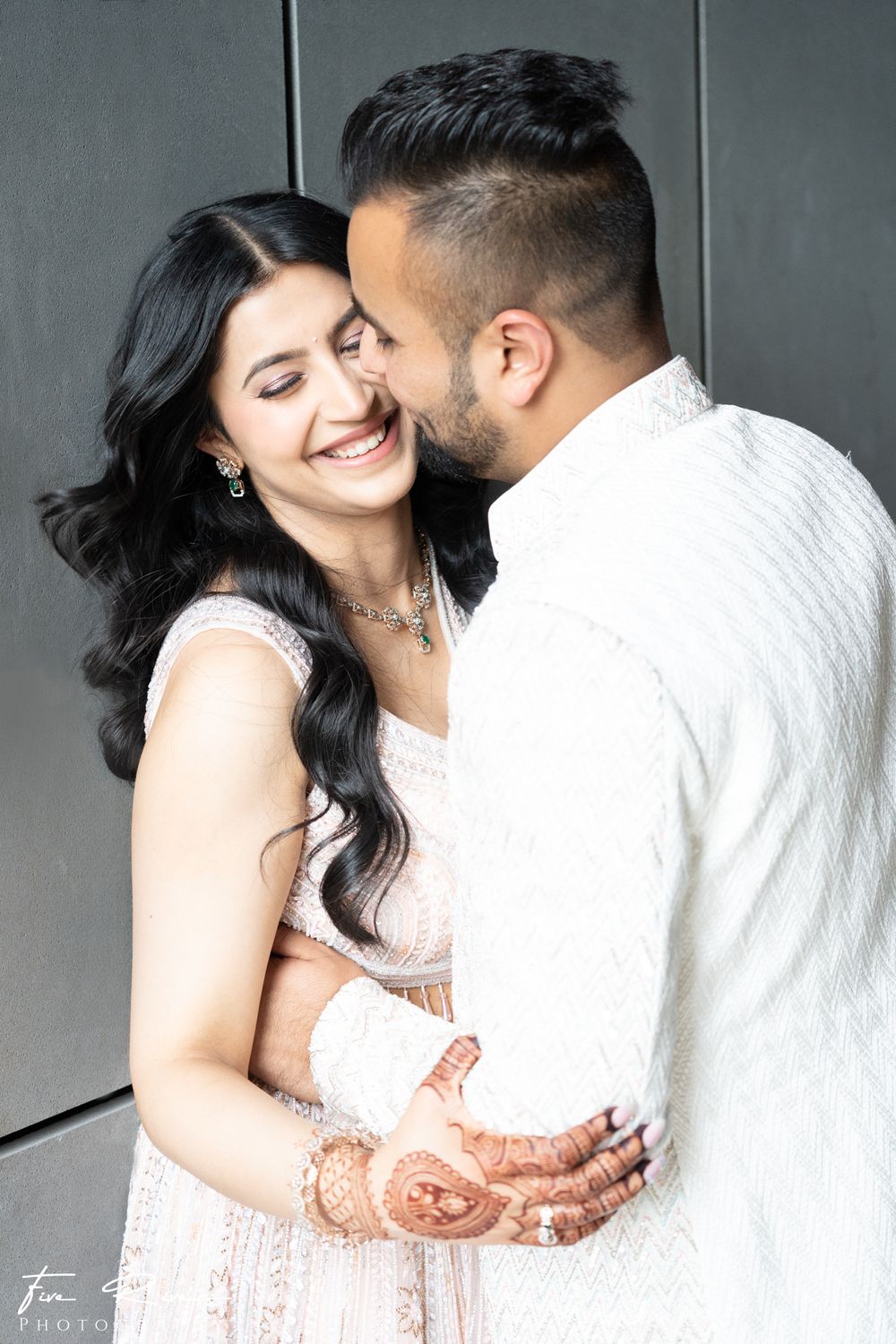 A romantic couple shares an intimate moment, with traditional henna designs visible on her hands as they embrace.