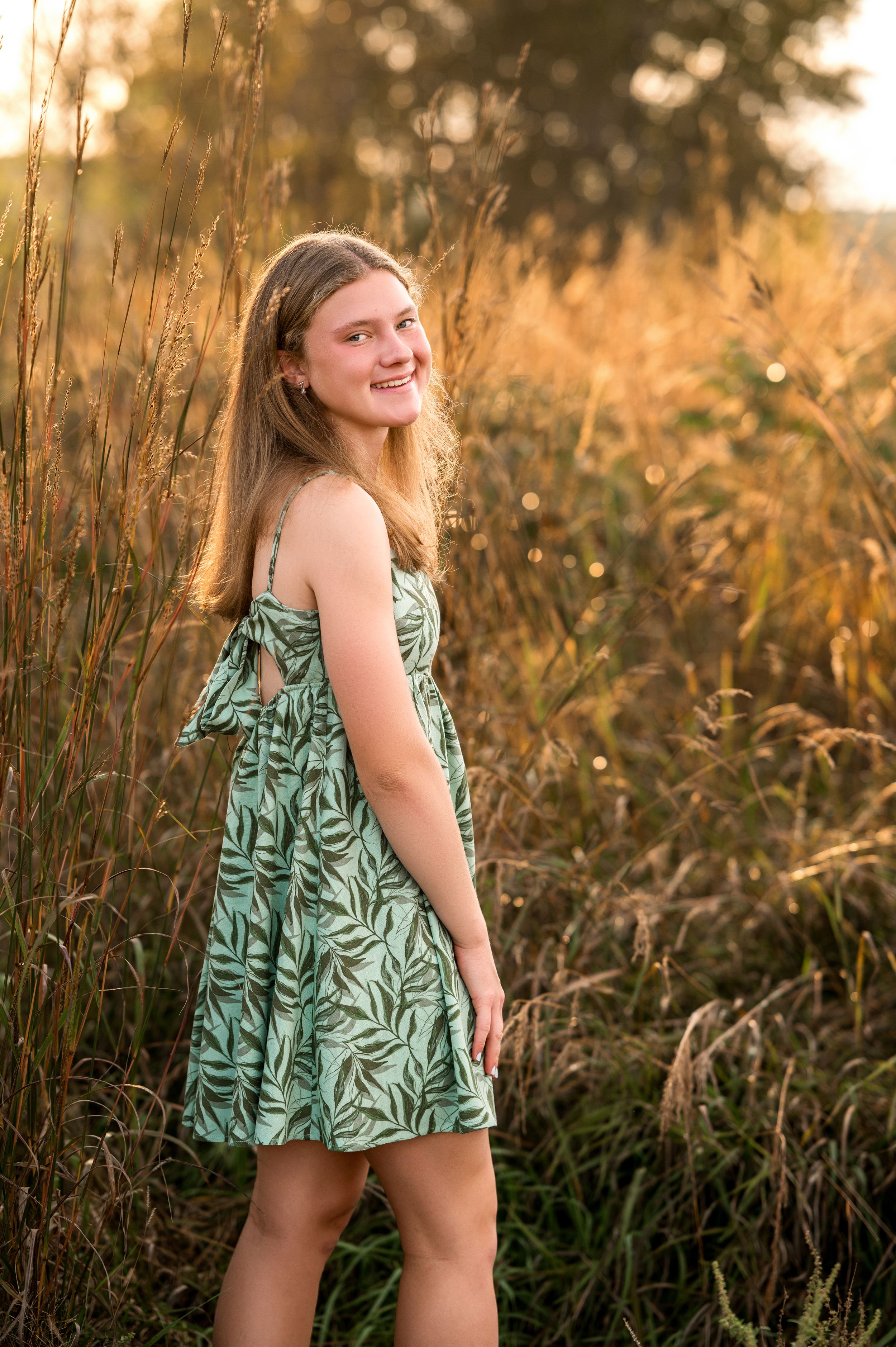 High school senior girl standing in tall grass at sunset, wearing a flowy dress – senior portrait session in Stillwater MN