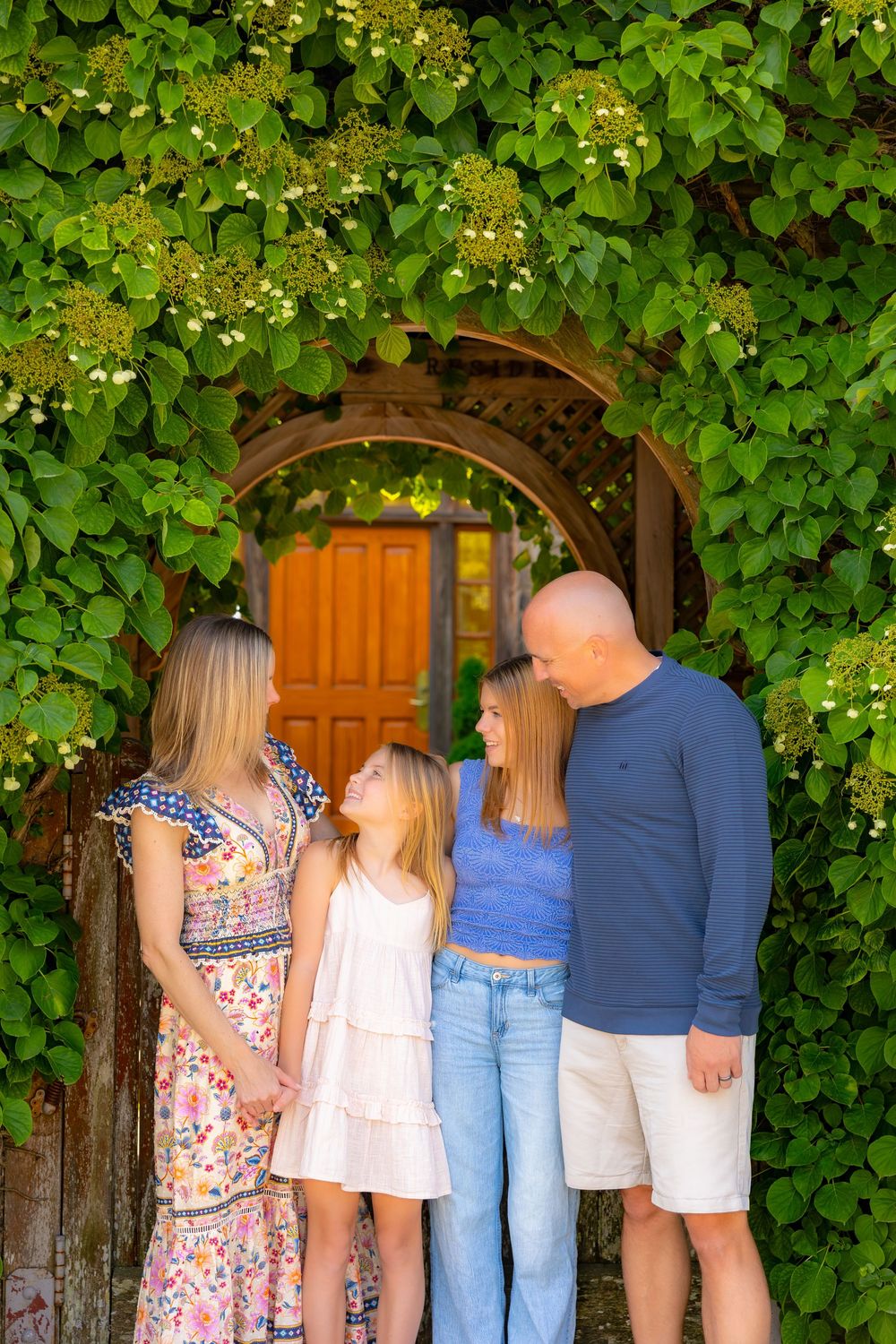 A group stands together in front of a wooden door surrounded by lush green foliage.