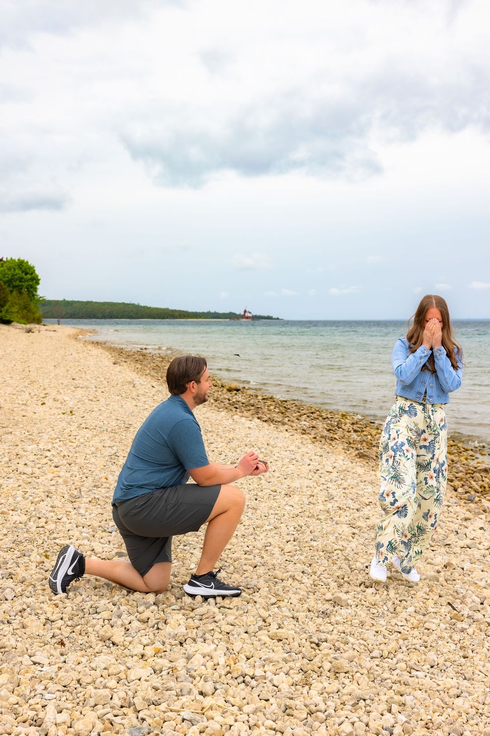 People taking photos on a rocky beach shoreline with water and cloudy sky in the background.