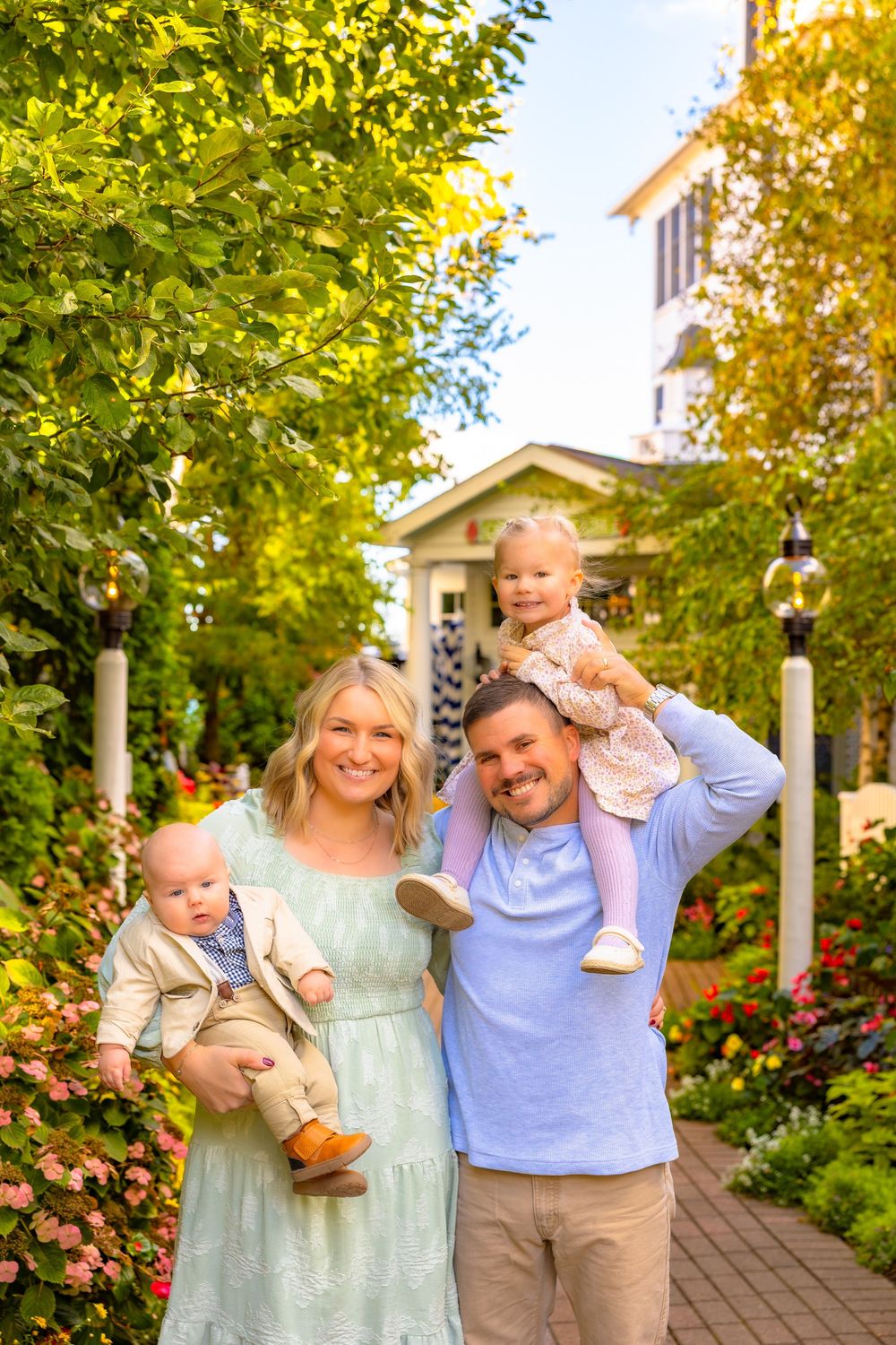 A family shares joyful moments together in a garden pathway surrounded by lush greenery and blooming flowers.