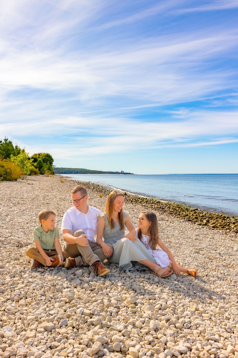 A group relaxes together on a rocky beach shore with blue water and sky on a sunny summer day.