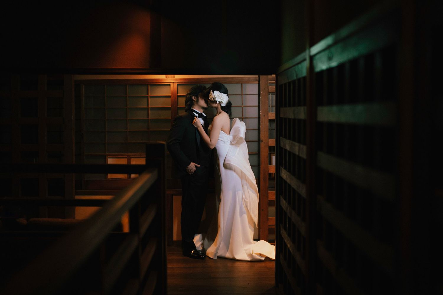 Romantic wedding couple sharing a kiss in a warmly lit wooden corridor during their reception.