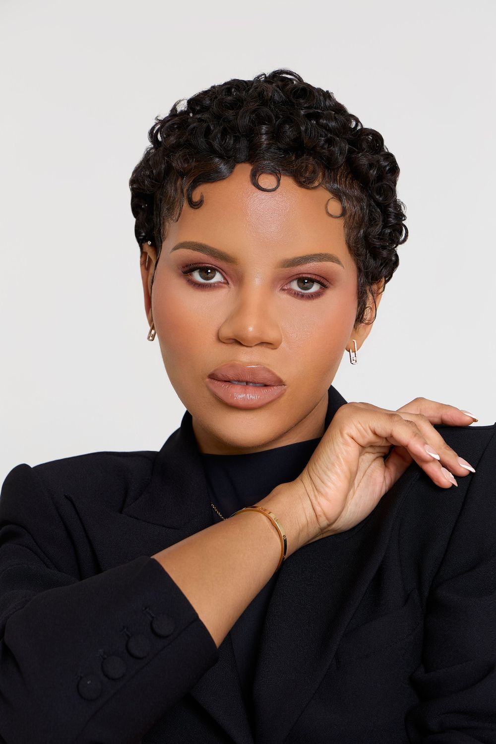 Series of close-up portraits of a person with short curly hair and black attire posing against a light background.