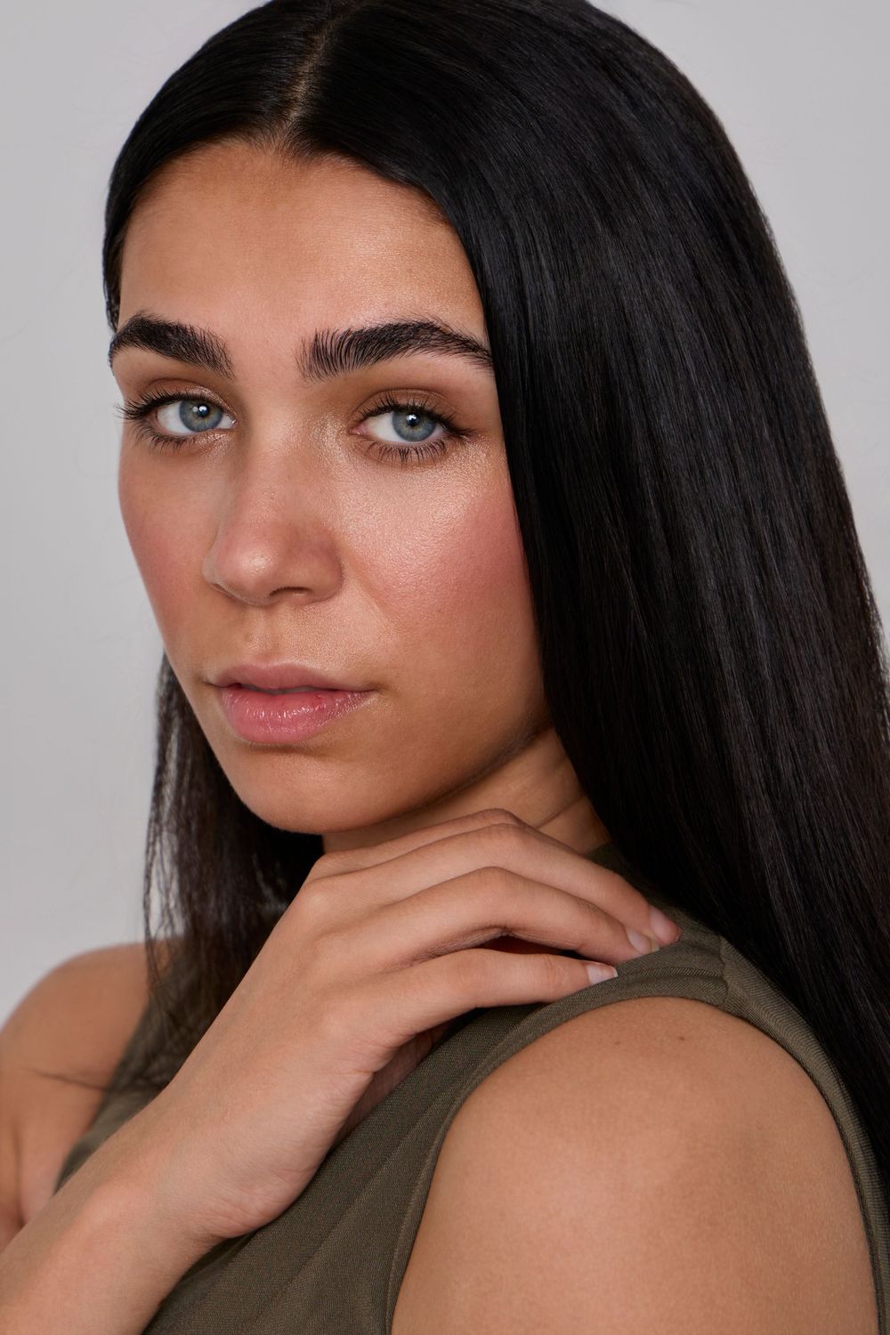 Studio portrait with olive green top against grey background.