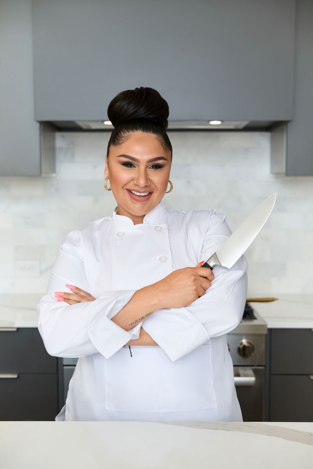 Chef in white uniform posing with knife in contemporary kitchen.