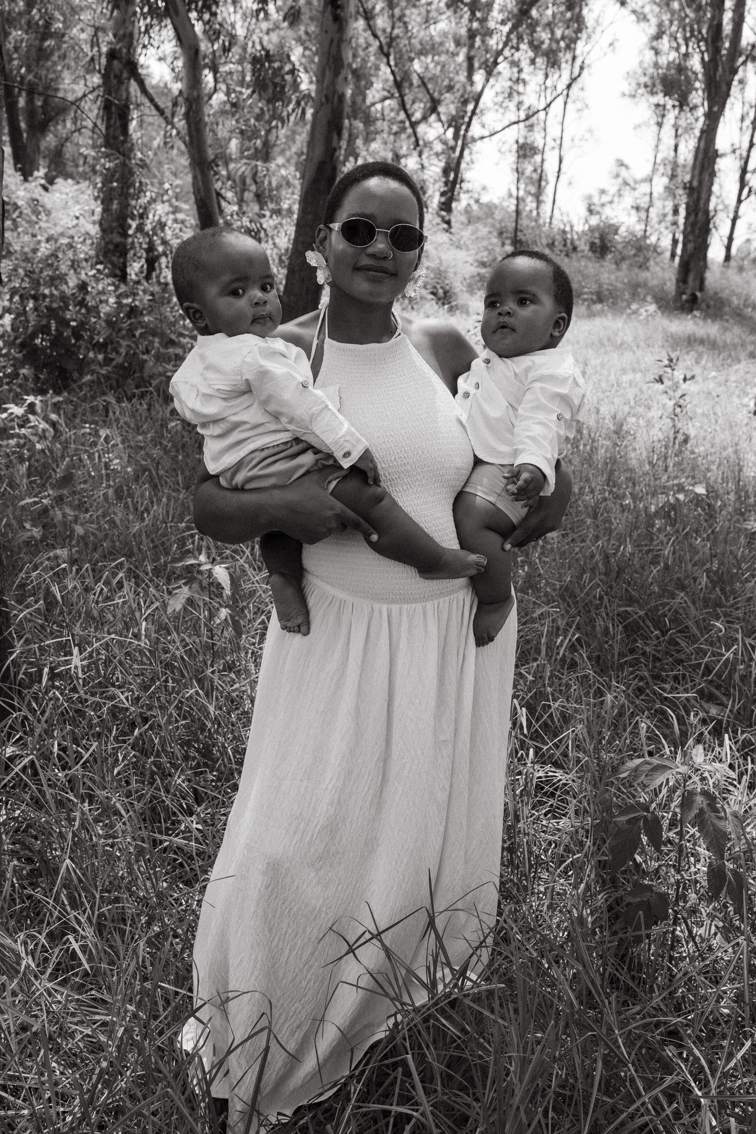 Black and white portrait of family members in flowing white dresses against natural backdrop.