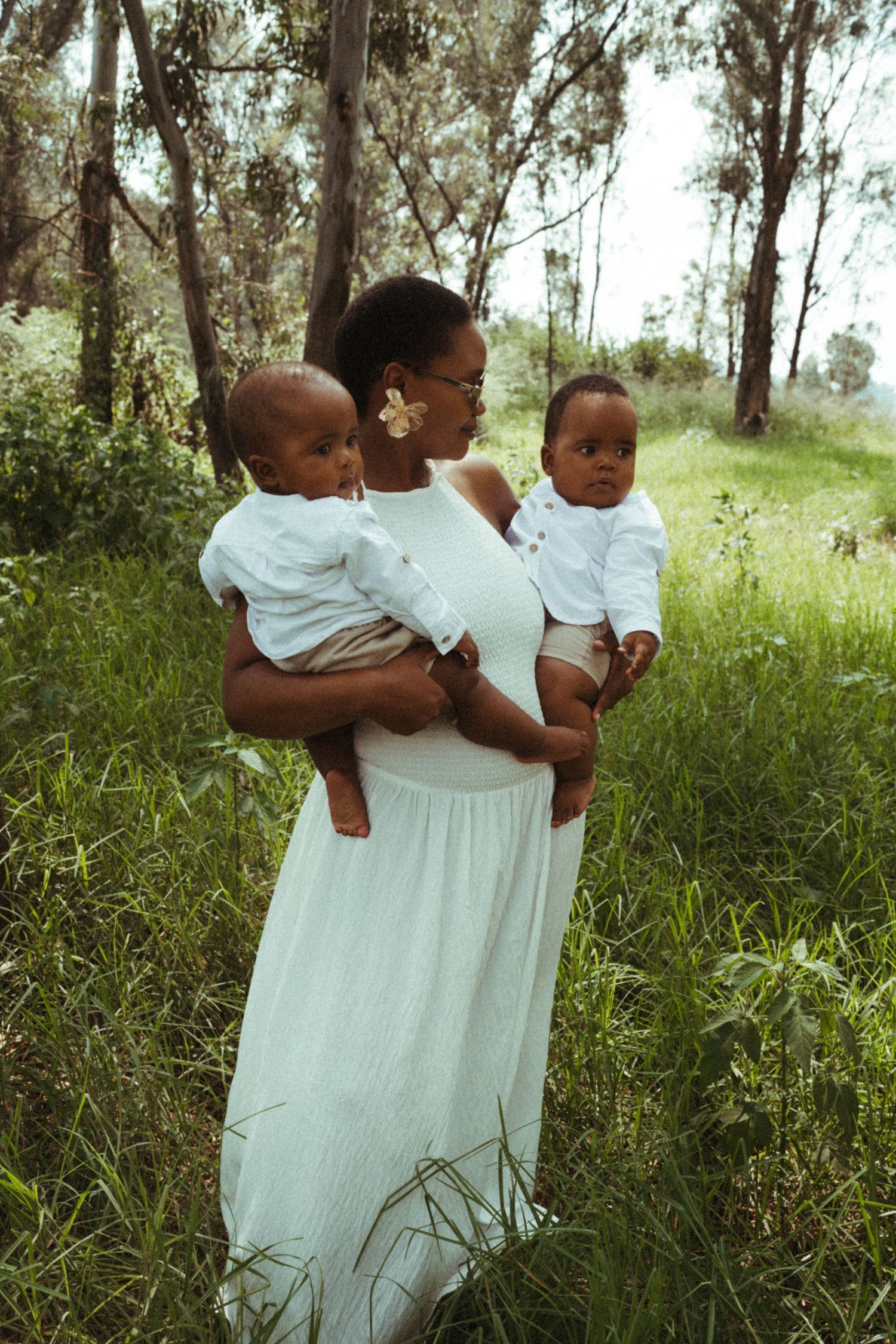 Family dressed in white poses together in a sunny outdoor field with eucalyptus trees.