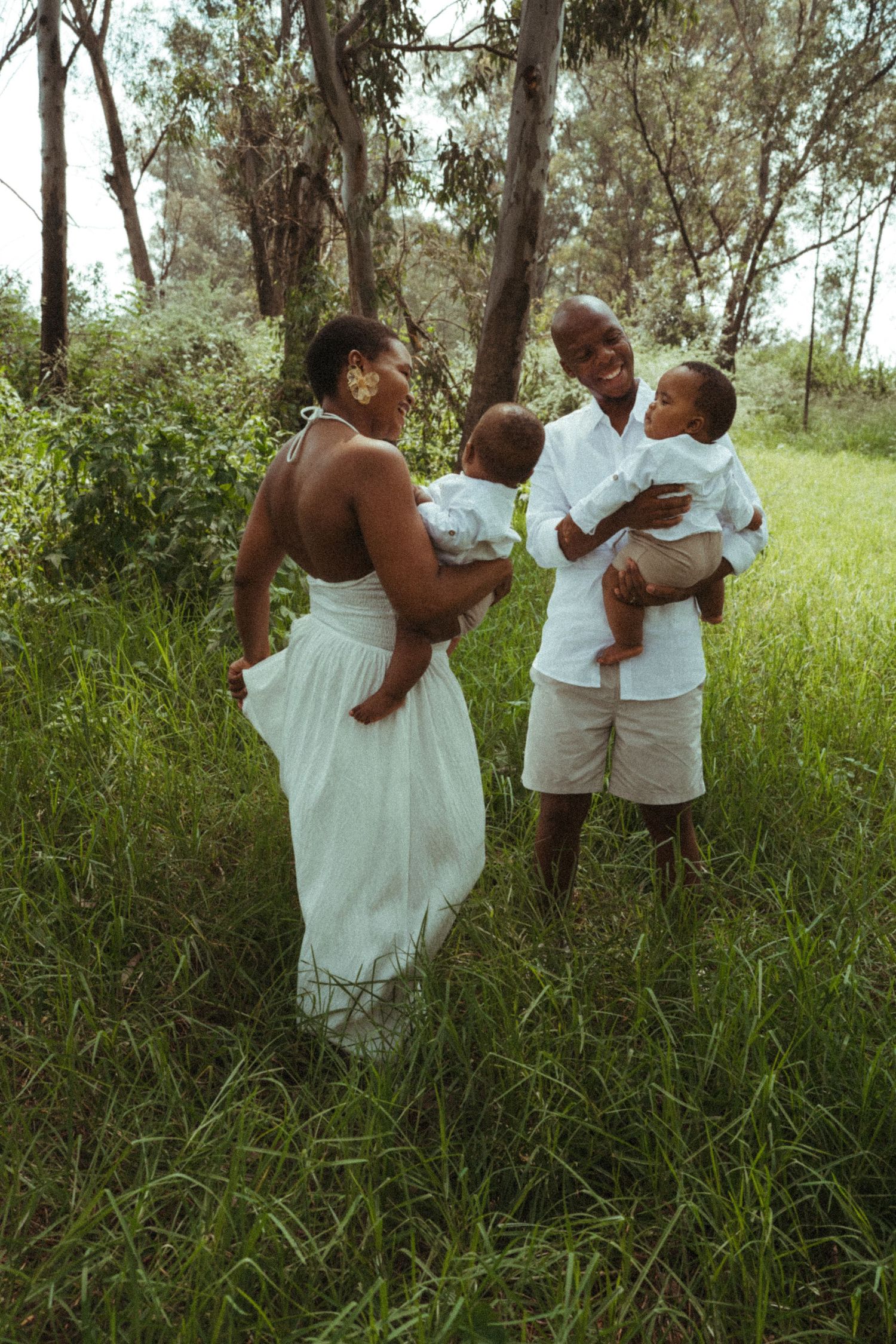 Family members share tender moments together in a wooded area while wearing coordinated white clothing.