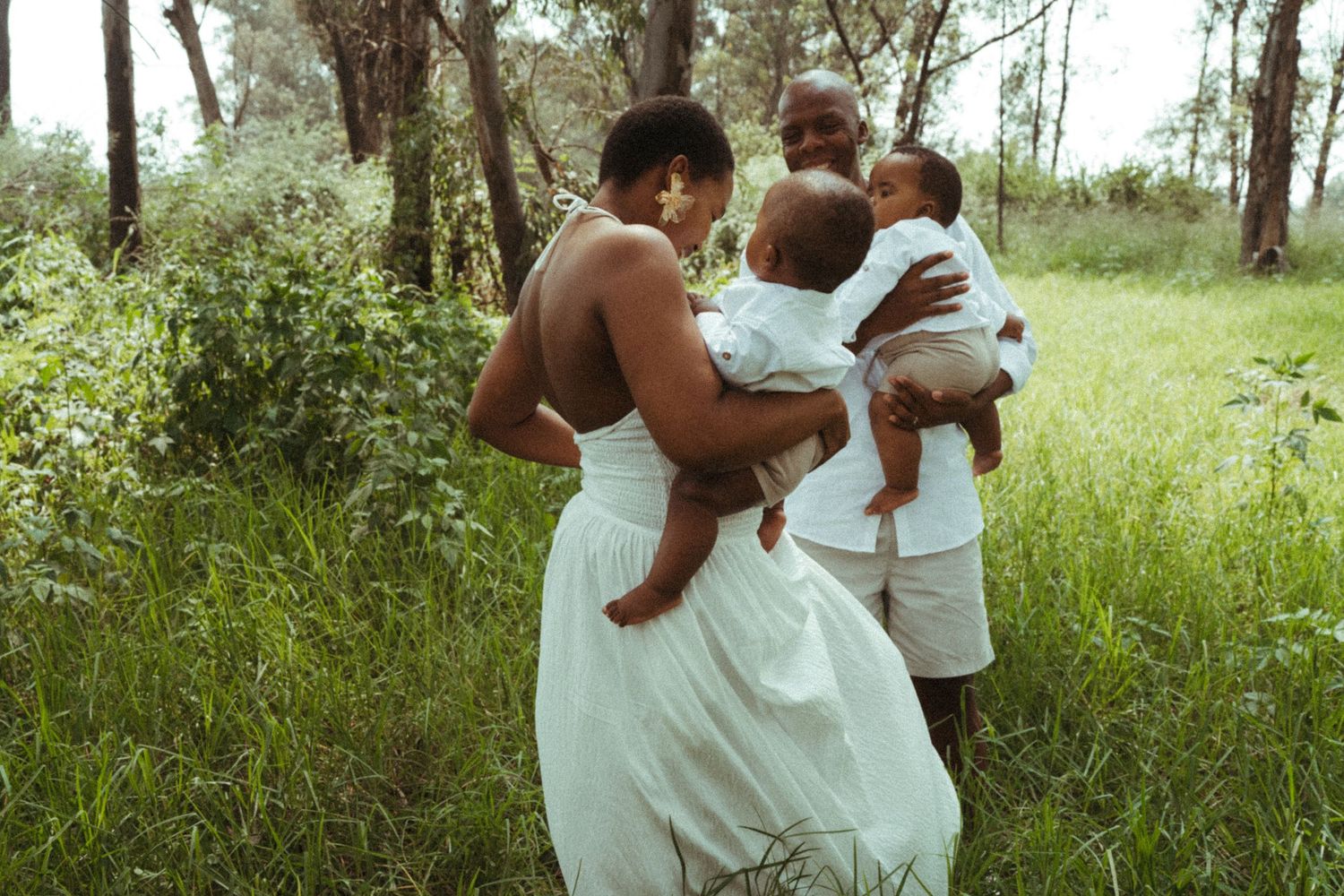 Family photoshoot in white attire against a backdrop of trees and wild grass.