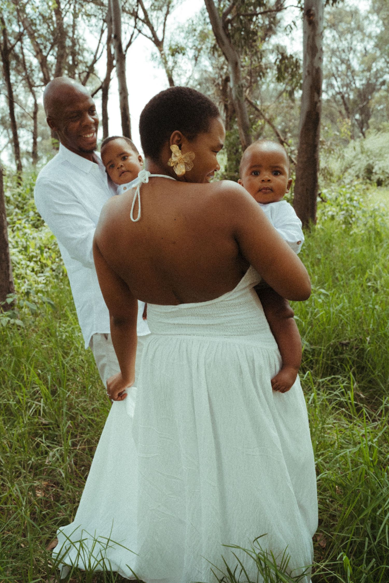 Family members in white dresses and shirts share joyful moments in a natural setting.