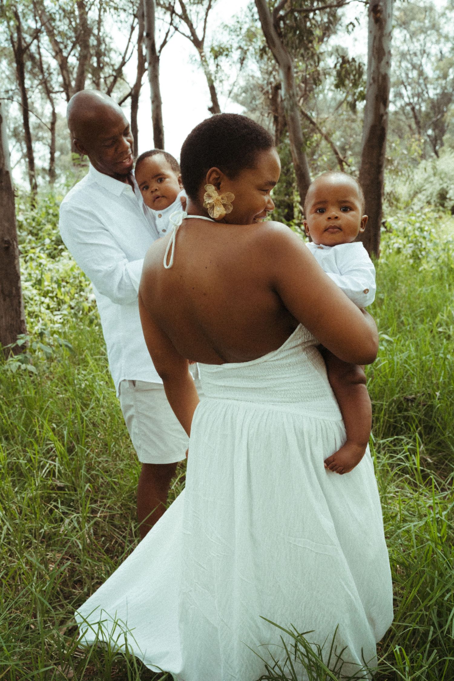 Candid family moments captured in white outfits against a backdrop of trees and grass.