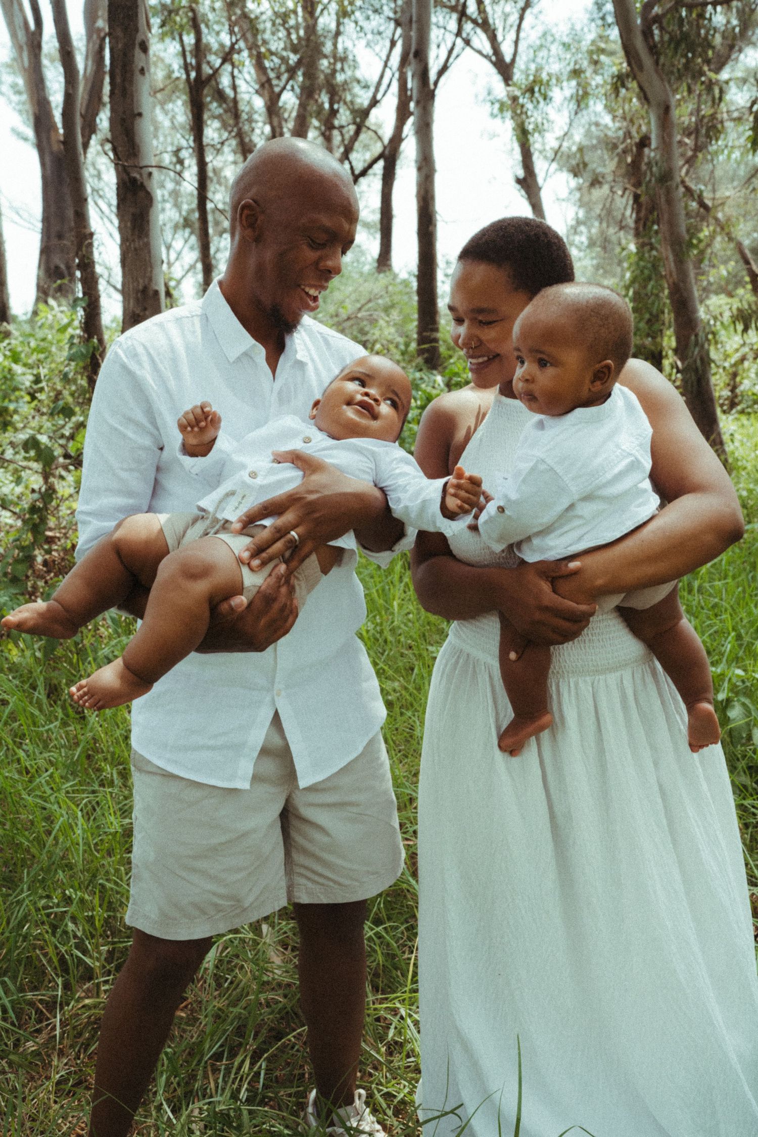 Playful family moments captured in white outfits among trees and tall grass.