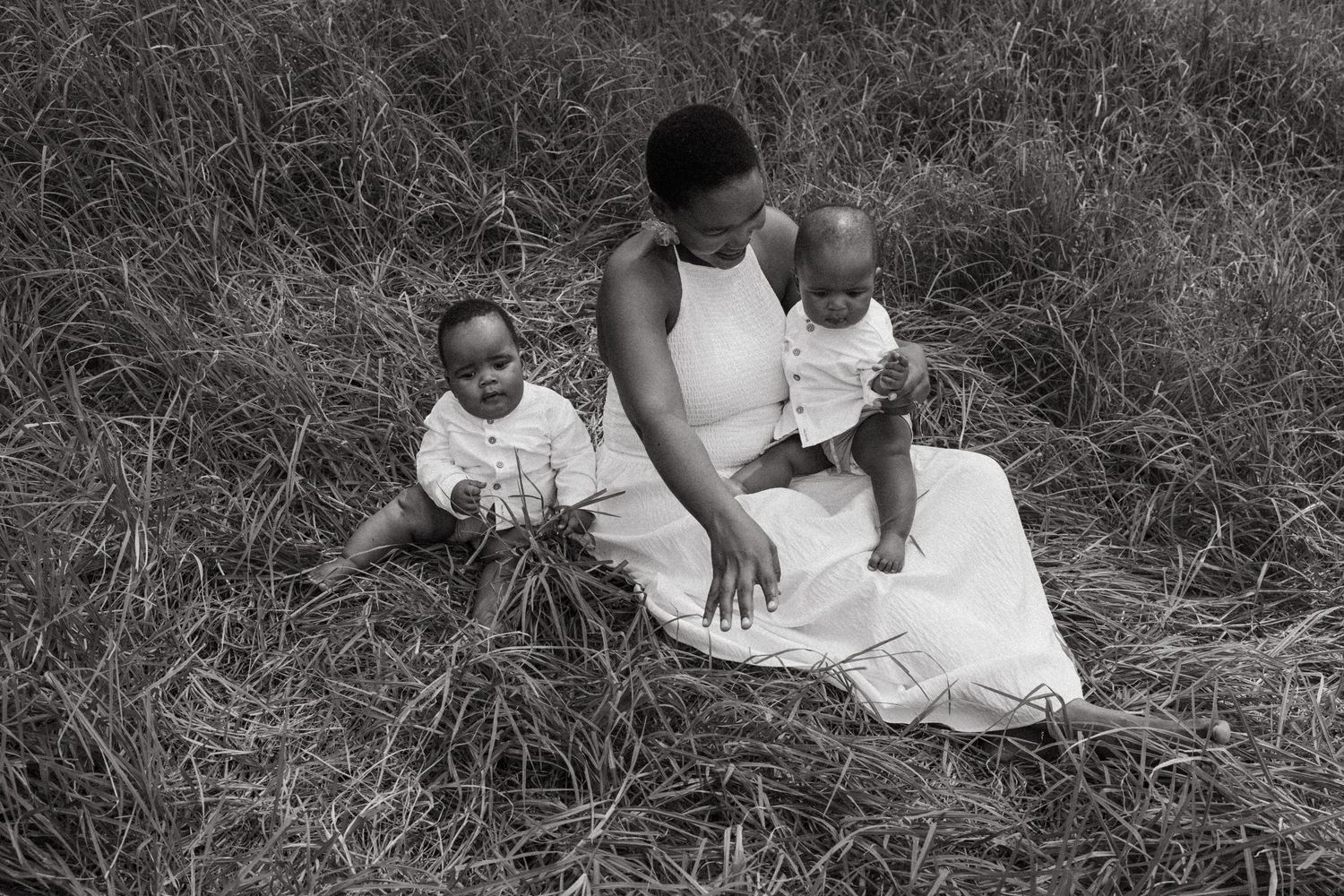 A family wearing white sits together on grass during an outdoor photo session.