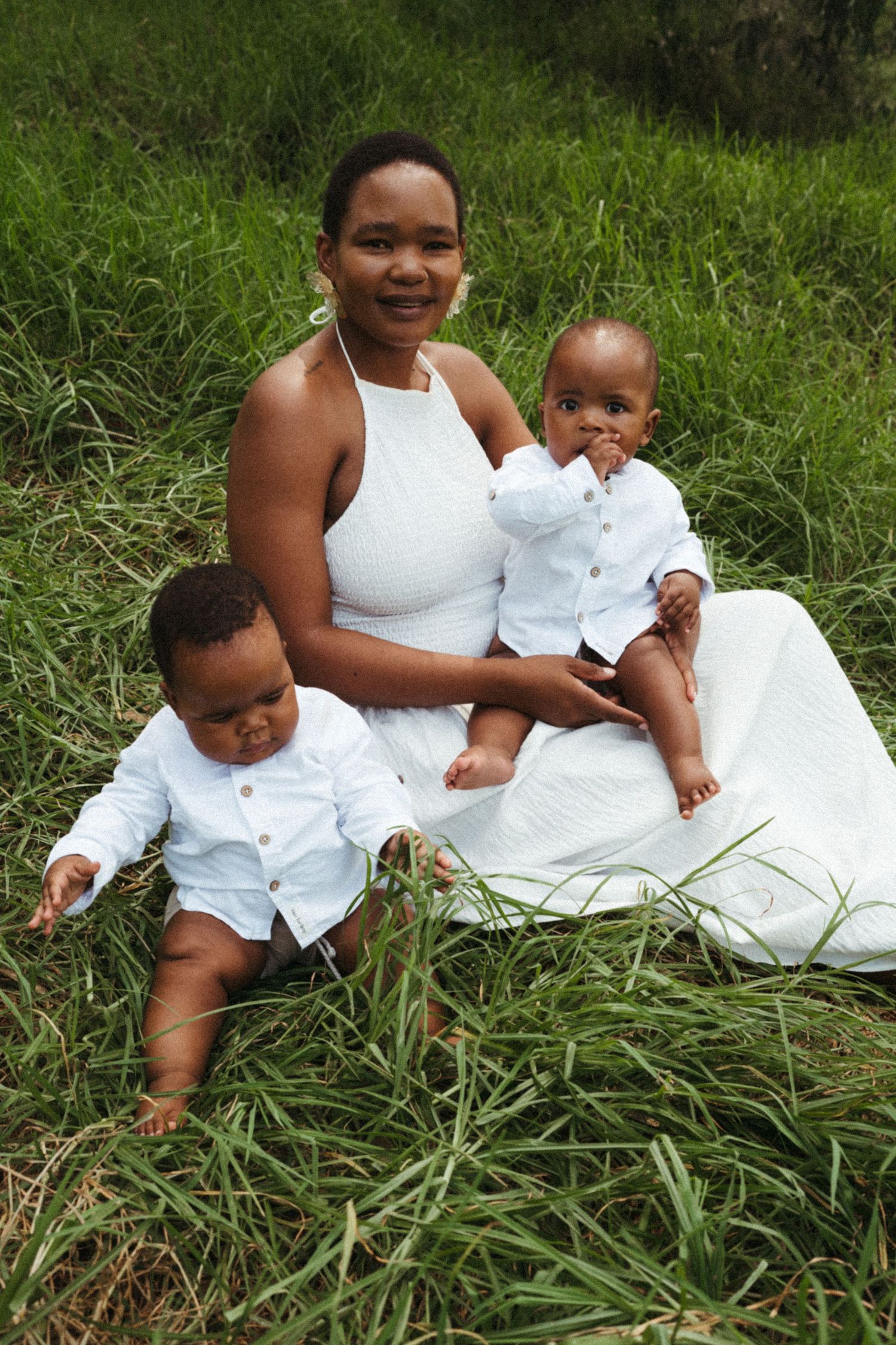A family in matching white outfits poses on green grass during a sunny day.