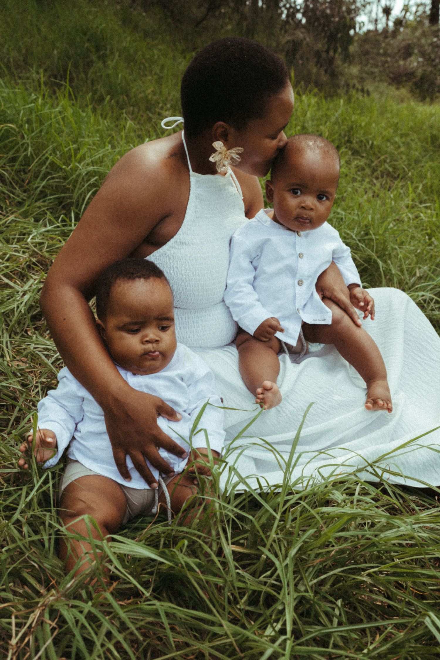 Close-up shot of a family in white clothing sitting among tall grass.