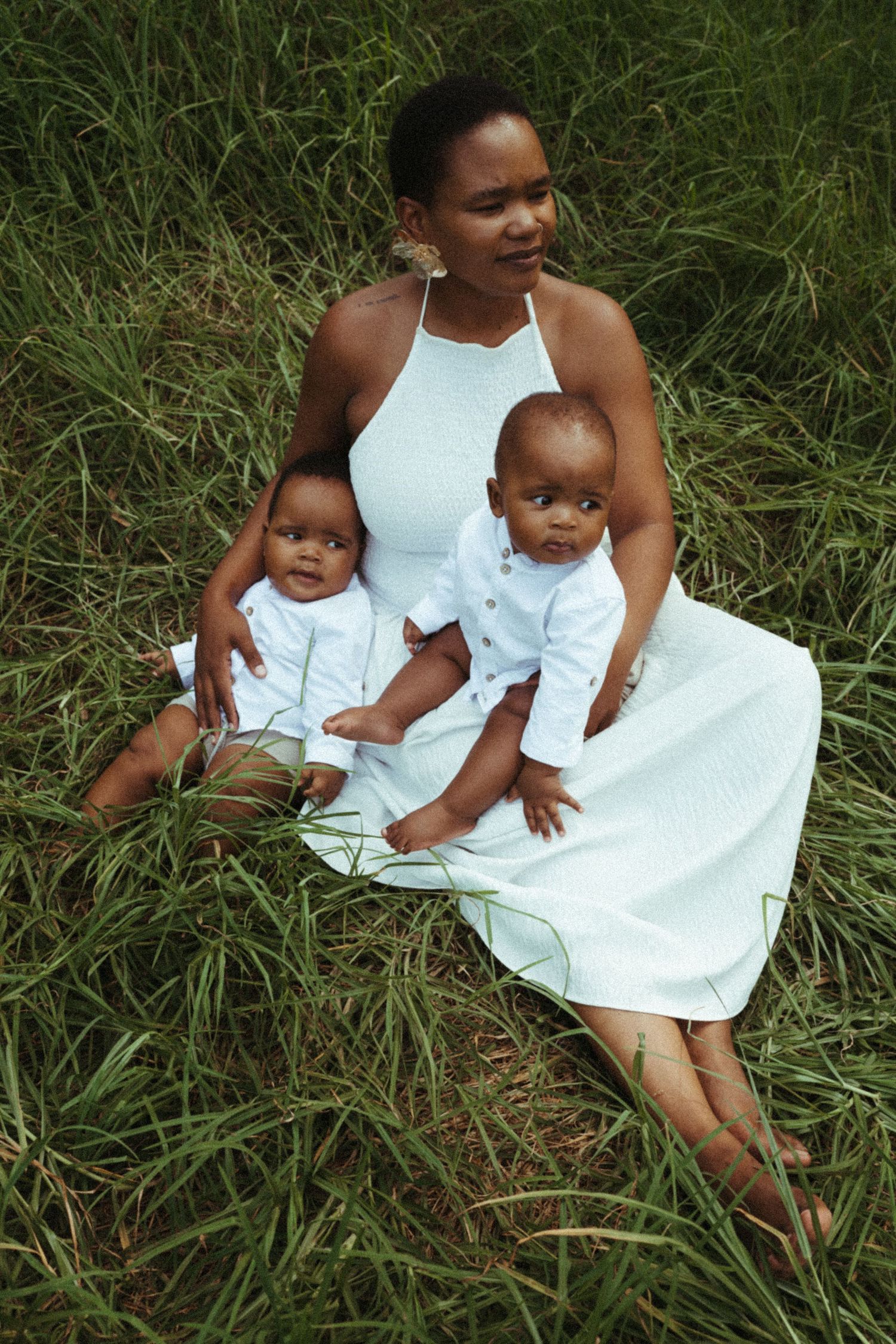 Family wearing coordinated white outfits poses together on grassy hillside.