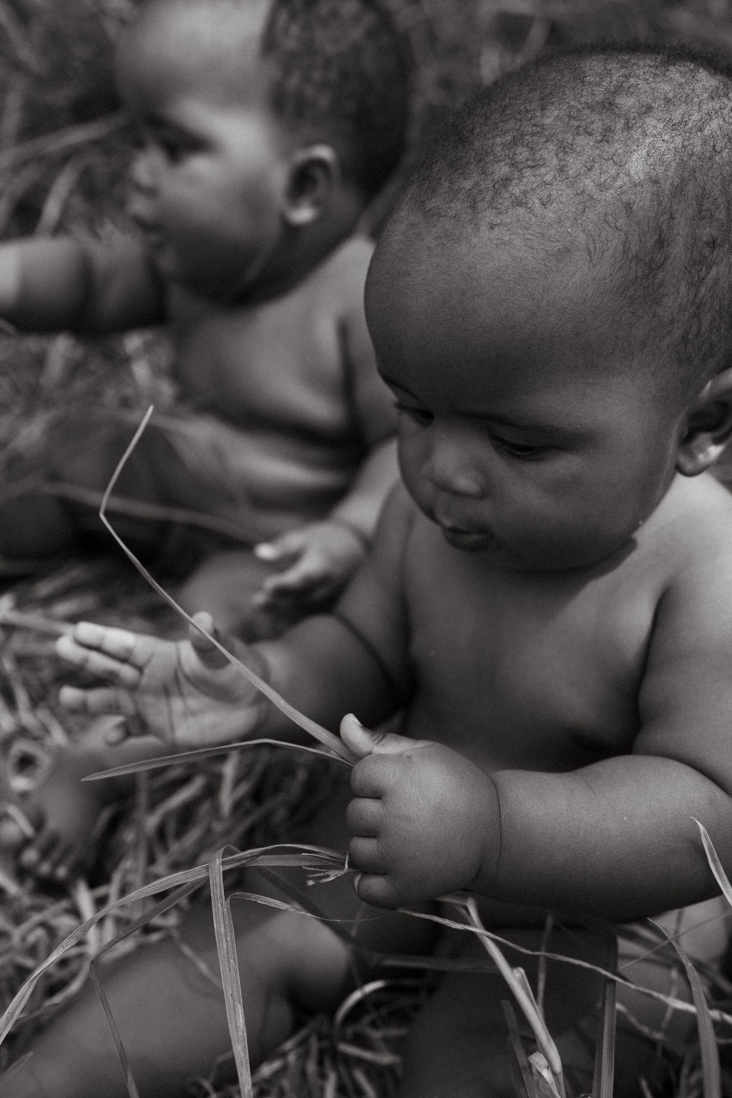 Black and white close-up of baby examining grass blades with curiosity.