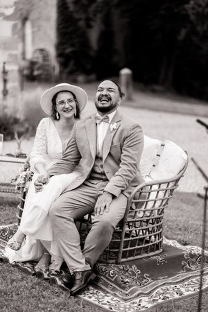 Bride and groom share candid laughter while sitting together on an ornate blanket outdoors.