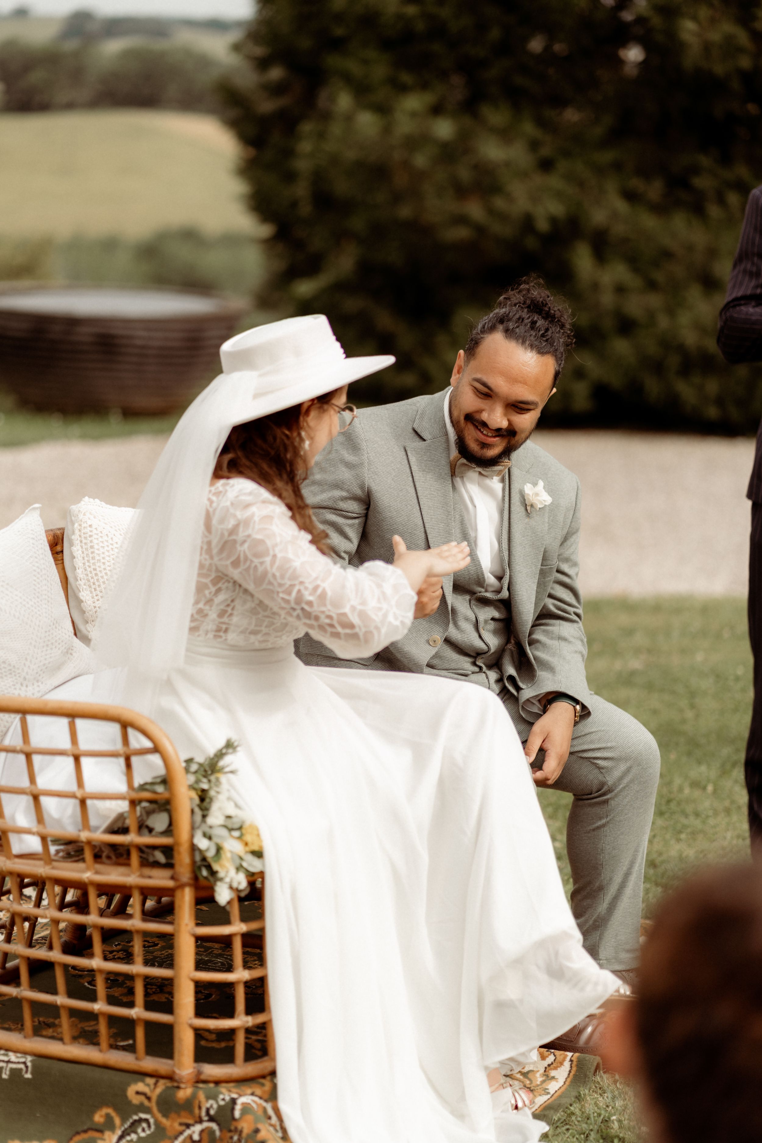 A couple shares a candid laughing moment while seated in a wicker chair during their outdoor ceremony.