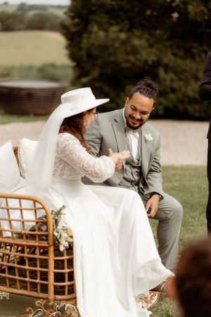 A couple shares a candid laughing moment while seated in a wicker chair during their outdoor ceremony.