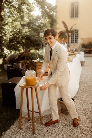Person in light colored suit pouring drinks at elegant outdoor wedding reception.