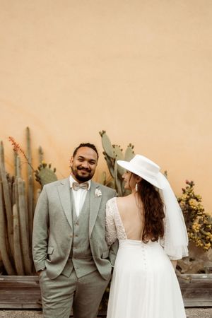 Desert themed wedding portraits with couple posing against beige wall and cacti backdrop.