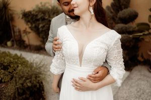 Close-up detail of an elegant white lace wedding dress with plunging neckline and three-quarter length sleeves.