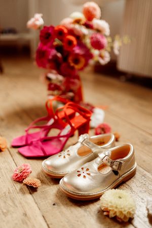 A pair of silver metallic Mary Jane shoes sits on a wooden floor with blurred red flowers in the background.