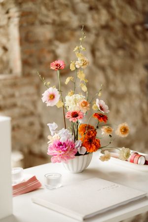 Pink and orange flowers in white vases create a soft and dreamy still life composition on a white surface against a textured wall.