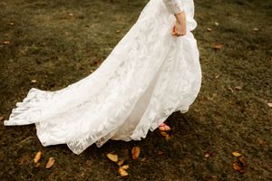 A flowing white lace wedding dress skirt billows over scattered autumn leaves on dark ground.