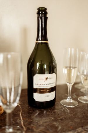 Multiple wine bottles and clear glasses line up against a dark marble countertop in a soft-focus composition.
