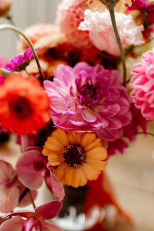 Close-up of vibrant pink dahlias, orange calendulas and red poppies in a soft-focus floral arrangement.