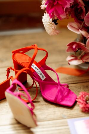 A pair of elegant pink and orange satin dance shoes with ankle straps arranged artistically beside delicate flowers.
