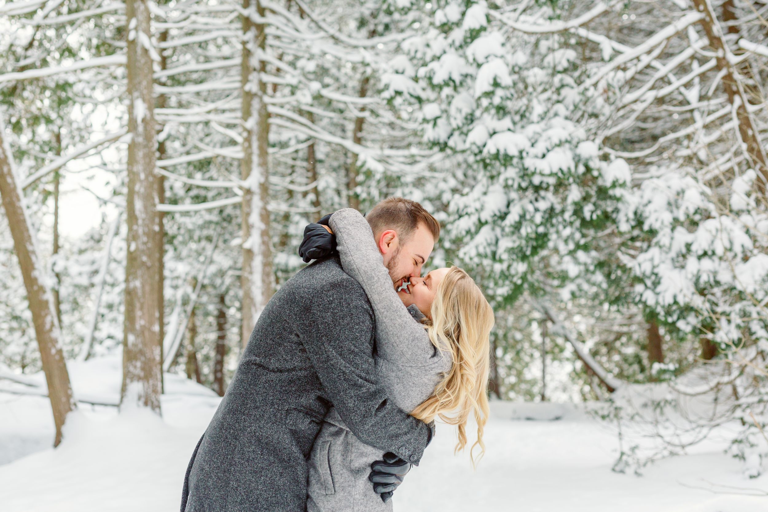 Couple shares intimate moment in snowy winter forest setting.