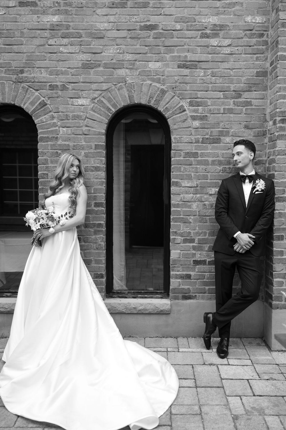 A sequence of wedding photos showing a bride and groom posing against a rustic brick wall in black and white style.