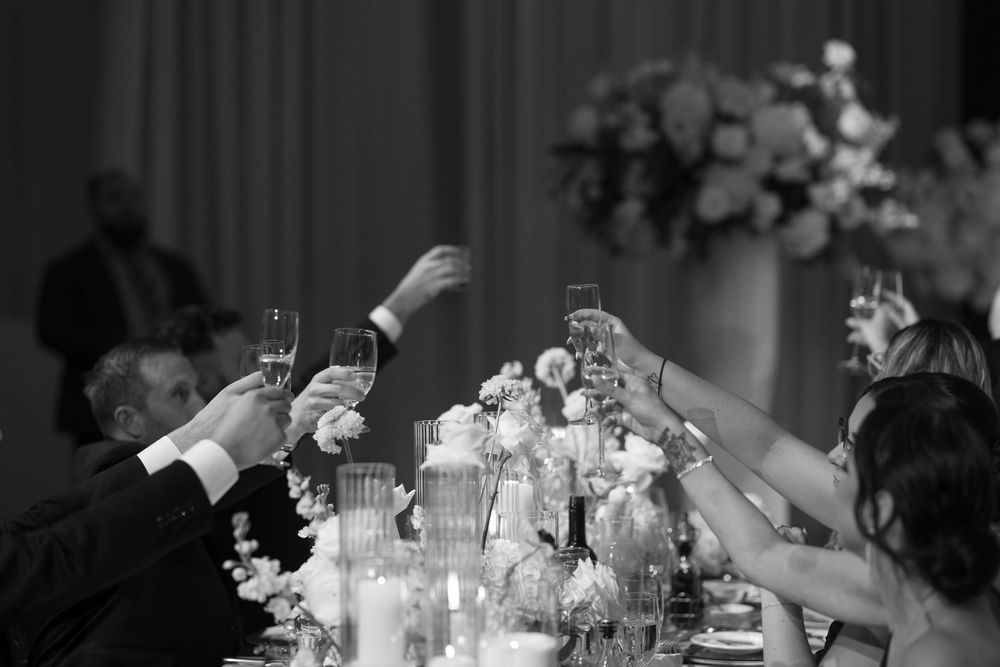 Wedding guests raise their glasses in a toast during an elegant reception dinner celebration.