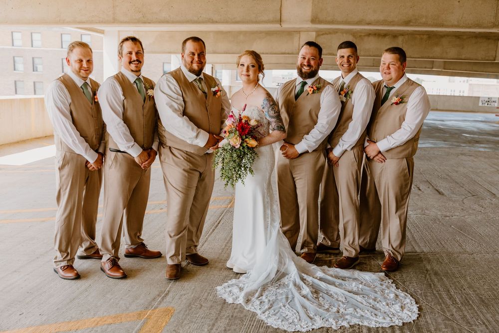 Wedding party poses together in formal attire on outdoor concrete platform.