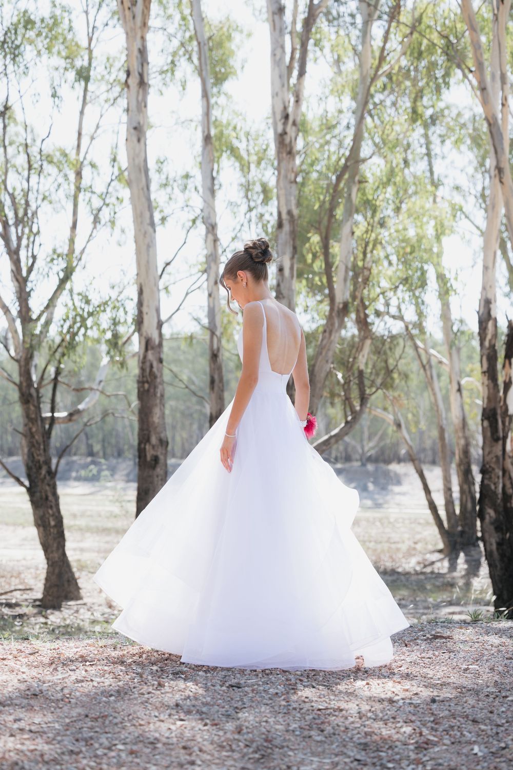 in white ballgown wedding dress standing among eucalyptus trees outdoors, holding red bouquet.