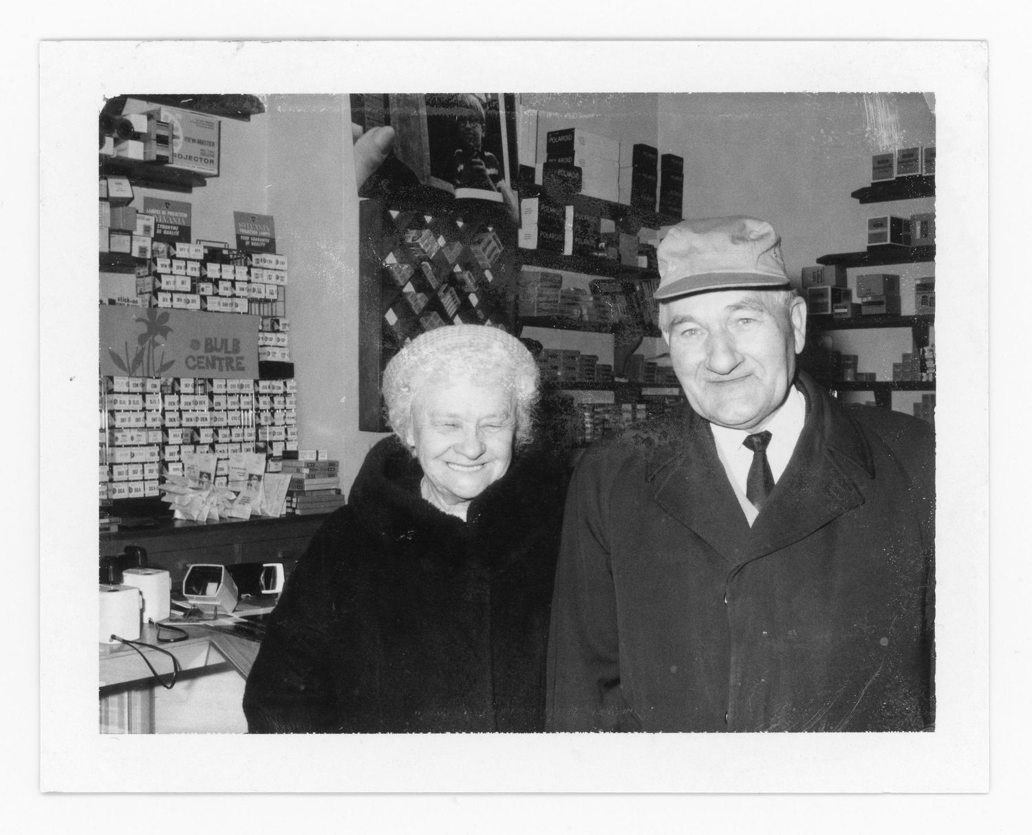 An elderly couple stands together inside a store with shelves of merchandise visible in the background.
