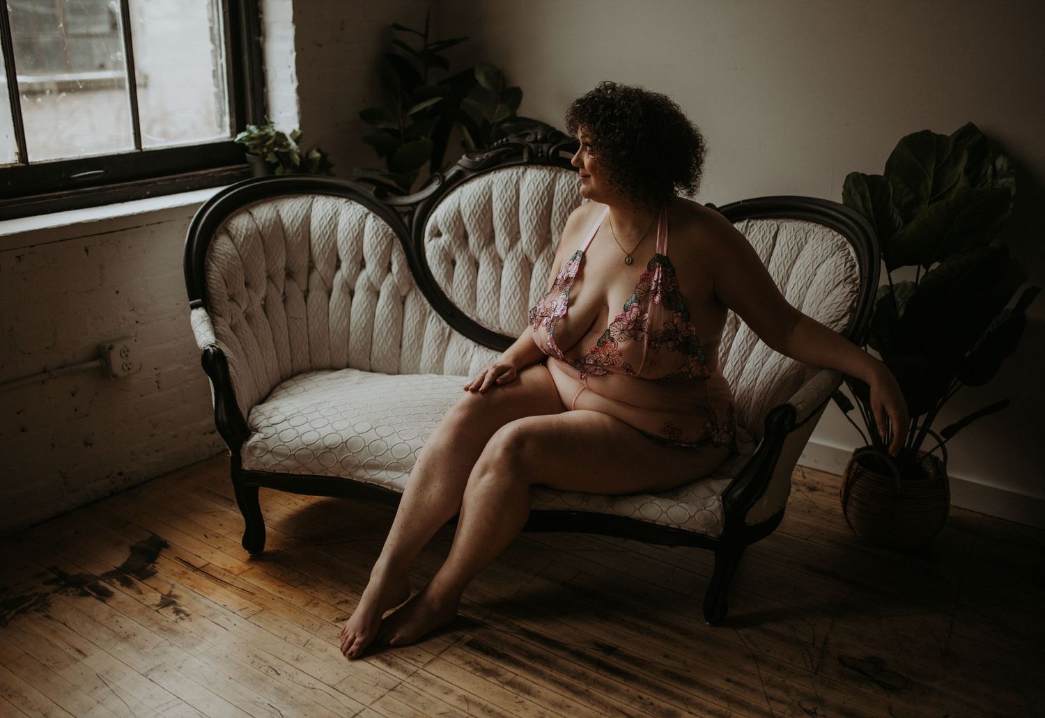 Artistic nude portrait on antique Victorian sofa near window with houseplants.