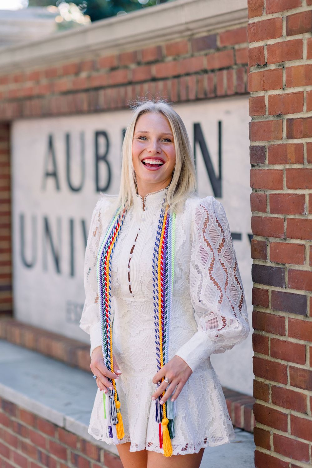 Stylish white lace top paired with colorful suspenders against a brick wall backdrop.