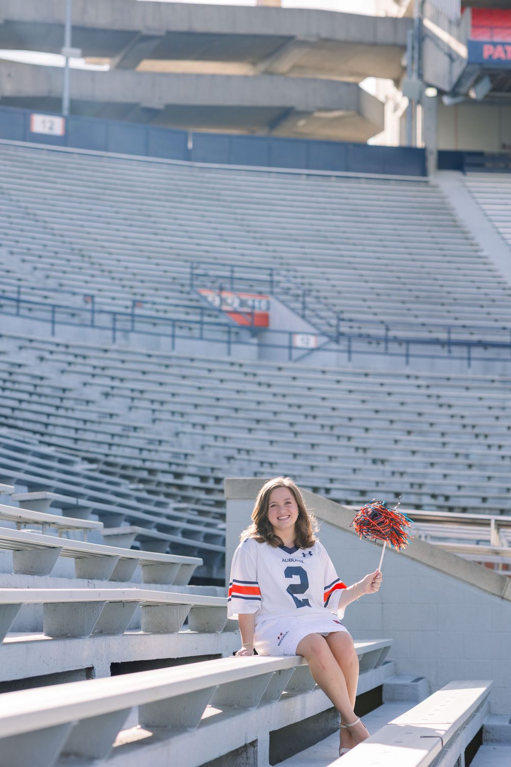 Graduate seated in empty stadium bleachers during photo session.