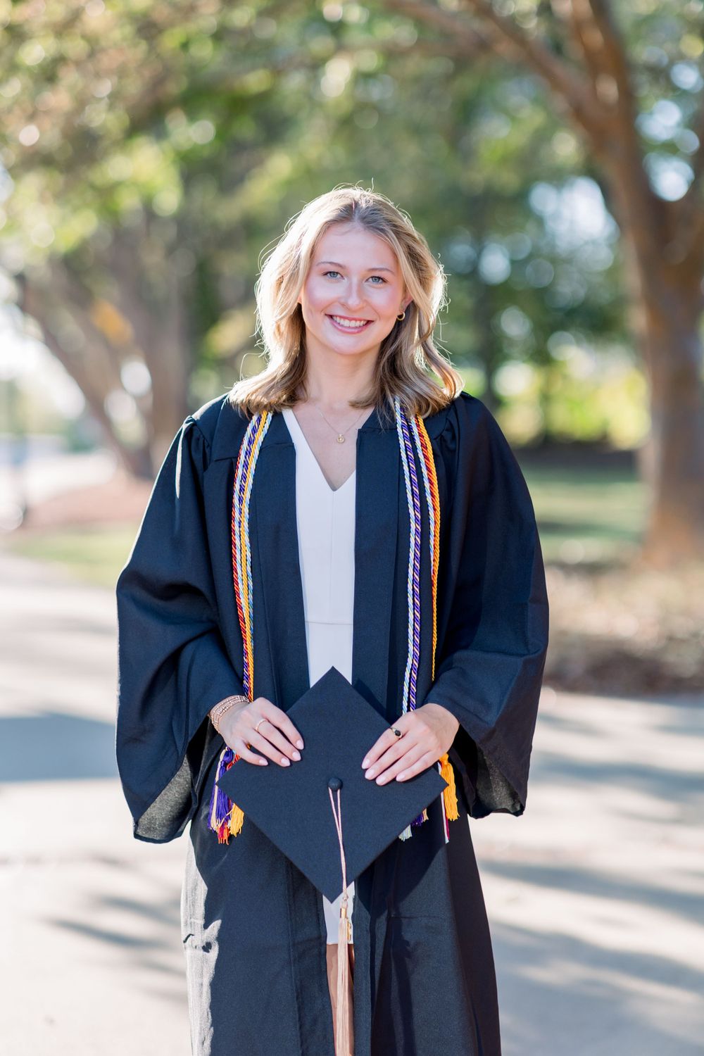 Graduate in traditional black graduation gown and colorful stole holds decorated mortarboard.