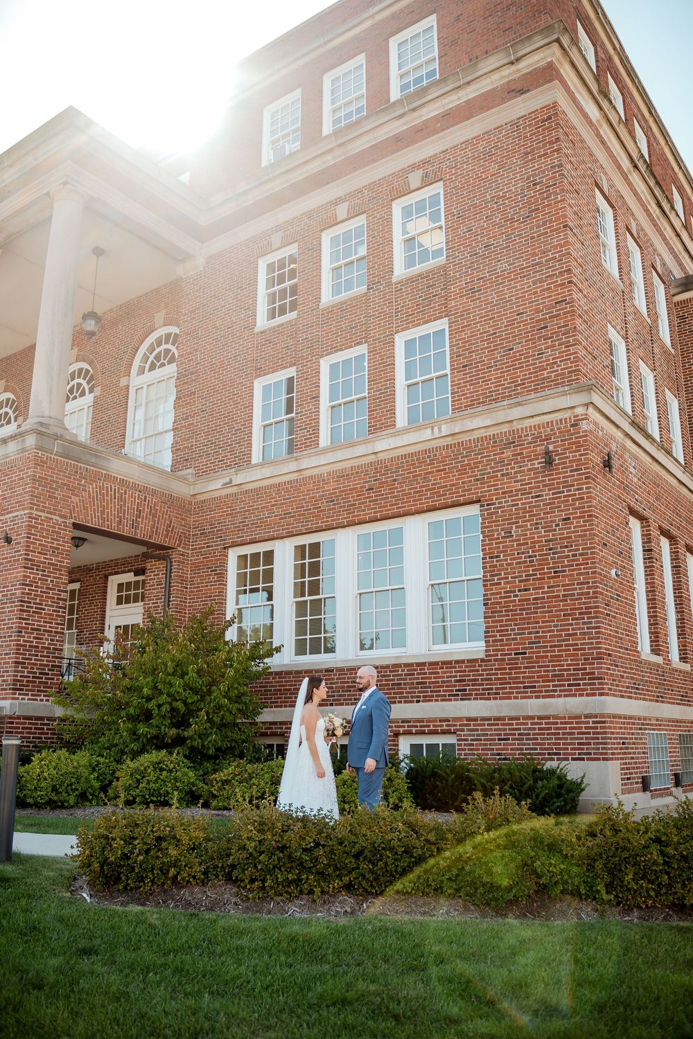 Classic red brick building with arched windows and landscaped grounds on a sunny afternoon.