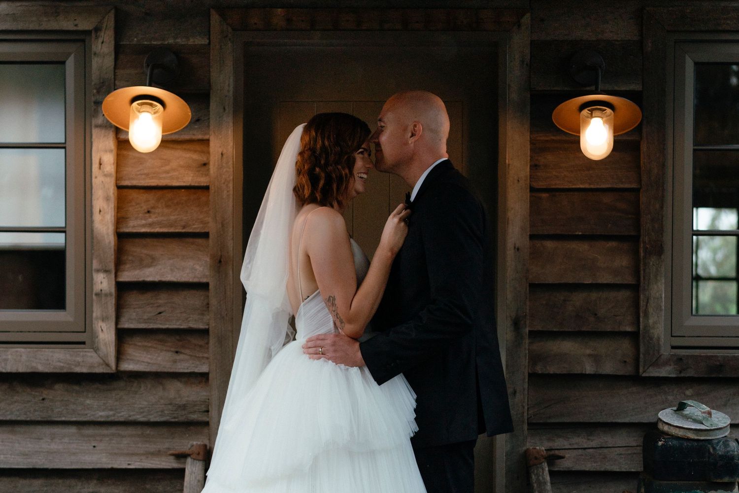 A romantic wedding moment shared between a couple at a rustic wooden cabin with glowing lantern lights.