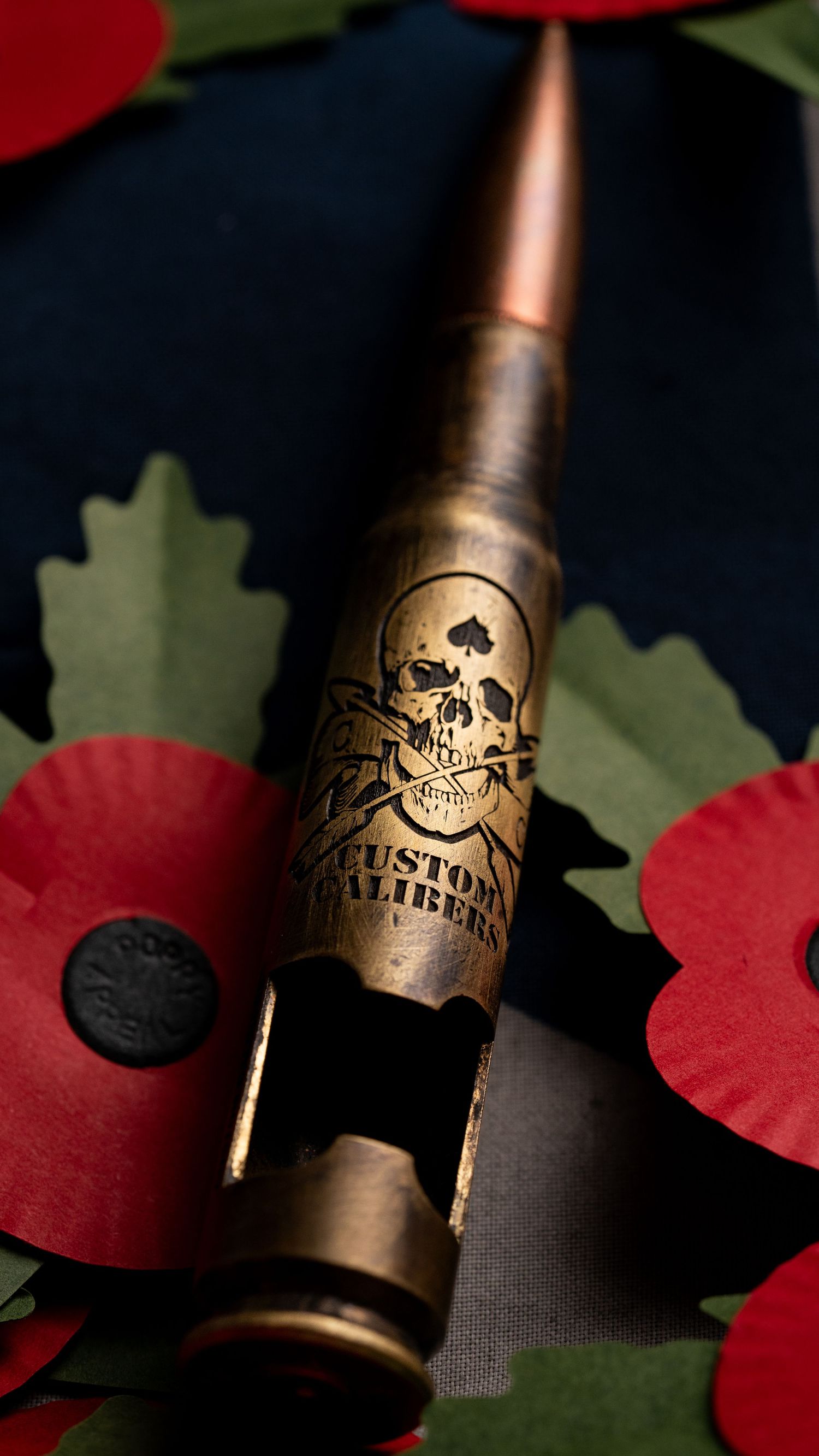 Custom engraved bullet with skull design amongst red poppies and green leaves.